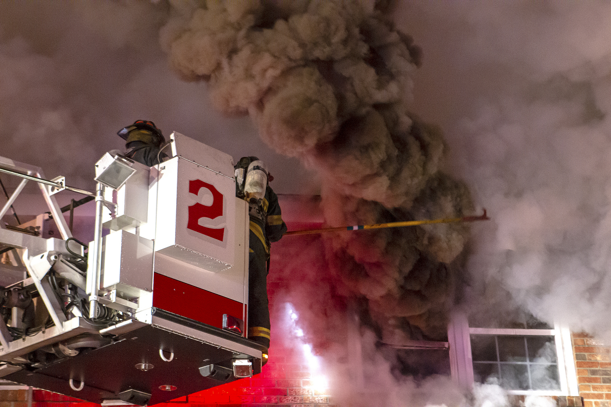 Image of a fire fighters at the top of the fire truck's ladder at a fire scene.